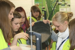 Die Mädchen füllen zum Deichbau groben Sand in die Versuchsrinne