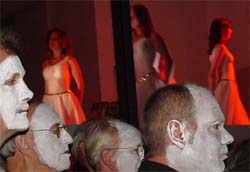 Tänzerinnen in rotes Licht getaucht, symbolisieren irdene Leichtigkeit, während weißgetünchte Sänger